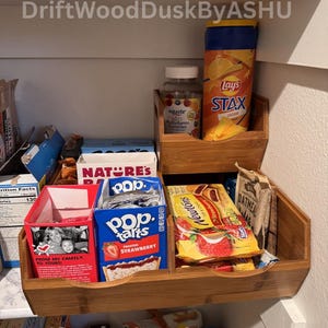 May include: A pantry shelf with bamboo organizers holding various food items. Includes Pop-Tarts, Lay's Stax, Nature's cereal, oatmeal packets, and Equate multivitamin gummies. The text "FROM MY FAMILY, TO YOURS!" is visible.