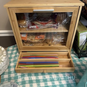 May include: A bamboo bread box with a clear glass door and a pull-out drawer. The box is filled with bread products and colorful straws. The text "DriftWoodDuskByASHU" is visible on the top and bottom of the image.
