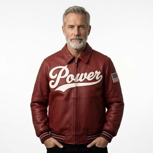 Puede incluir: Una chaqueta de cuero color burdeos con una aplicación en letras blancas que dice Power en el pecho. La chaqueta tiene un cuello clásico, una cremallera frontal completa y puños y dobladillo acanalados con rayas negras y blancas. Un pequeño parche de la bandera estadounidense se encuentra en la manga.