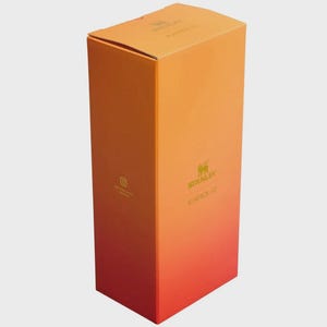 May include: A tall, rectangular cardboard product box featuring a vibrant orange-to-red gradient color scheme. The front displays the Stanley logo and the text KAROL G in gold lettering, with a small Instagram icon printed on the side panel.