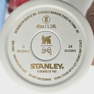May include: The circular base of a cream-colored tumbler features gold text and icons. It displays '40oz / 1.18L', 'STANLEY A BRAND OF PMI', 'DESIGNED IN SEATTLE WA ETHICALLY MANUFACTURED IN CHINA', 'BPA FREE', 'DISHWASHER SAFE', and a bear with wings icon.