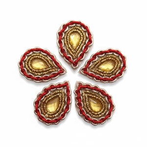 May include: Five teardrop-shaped fabric appliques. Each applique features a central yellow gem surrounded by gold beads, a silver border, and a red chain stitch edge. The appliques are arranged in a circular pattern on a white background.
