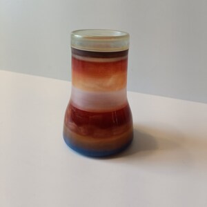 May include: A small, clear glass vase with a flared base and a wide mouth. The vase is decorated with horizontal stripes of brown, orange, white, and blue.