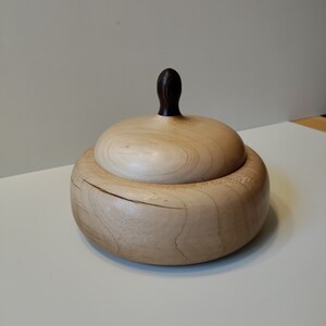 May include: A wooden box with a lid, made of light wood with a dark wood knob on the lid.