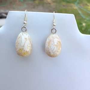 May include: A pair of white carved shell earrings with silver hooks. The earrings are oval shaped and have a delicate floral design.