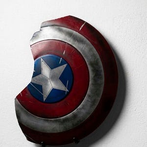 May include: A distressed Captain America shield, featuring a red, white, and blue color scheme. The shield has a star emblem at the center and shows signs of wear and tear, with a portion missing from the edge.