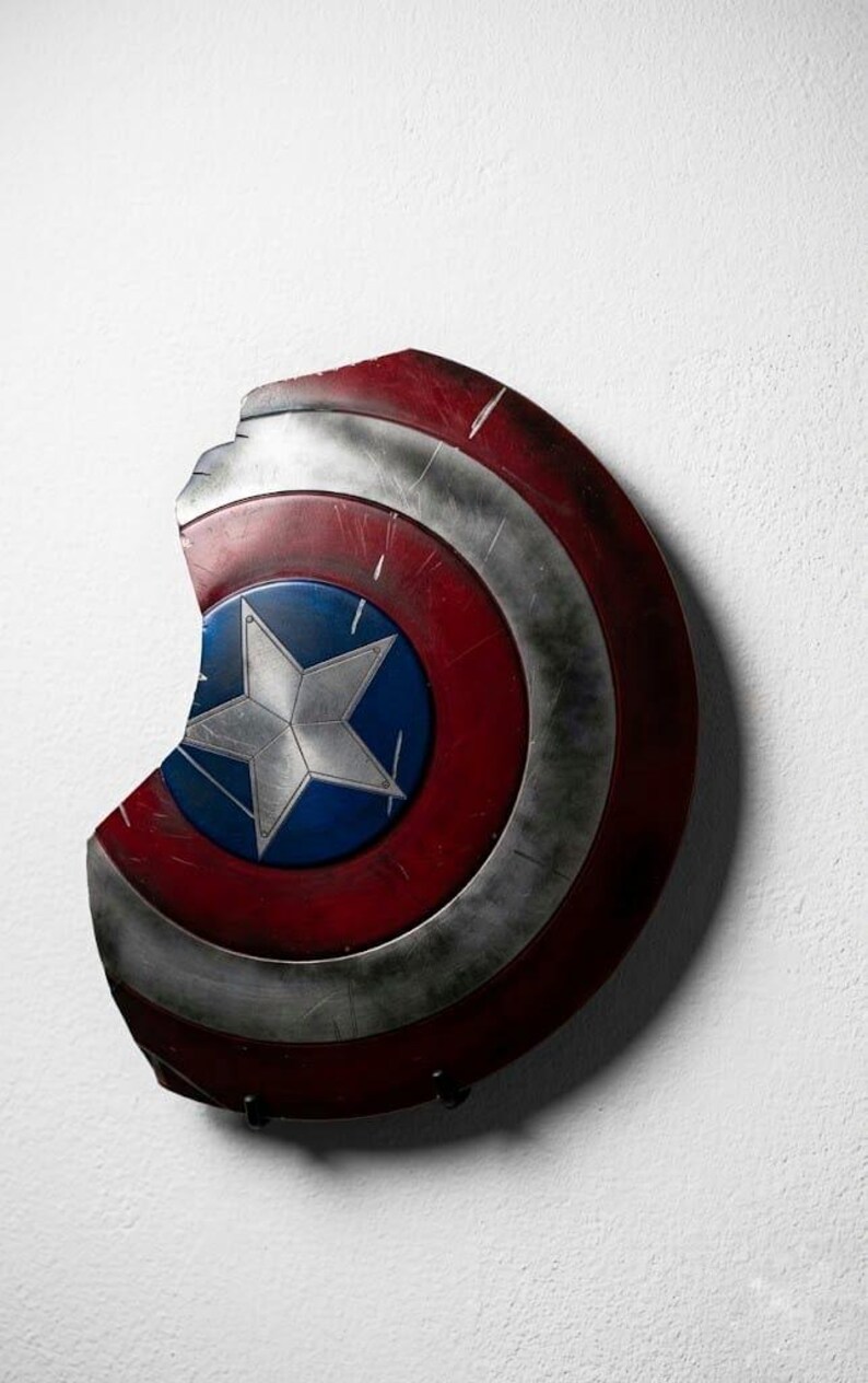 May include: A distressed Captain America shield, featuring a red, white, and blue color scheme. The shield has a star emblem at the center and shows signs of wear and tear, with a portion missing from the edge.