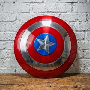 May include: A round, red and silver shield with a blue center and a silver star. The shield is made of metal and has a glossy finish. The shield is a replica of Captain America's shield.