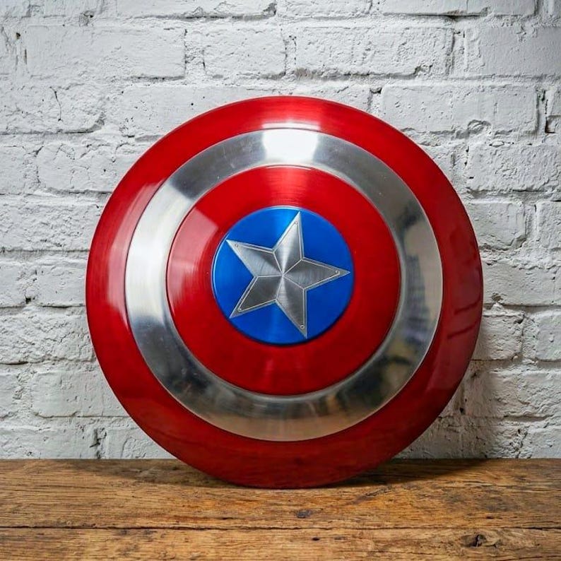 May include: A round, red and silver shield with a blue center and a silver star. The shield is made of metal and has a glossy finish. The shield is a replica of Captain America's shield.