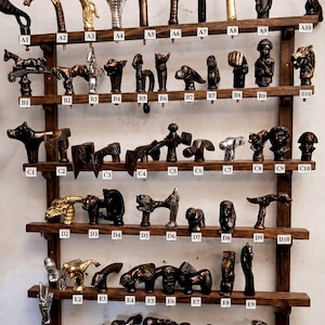 May include: A wooden wall-mounted display rack featuring six horizontal shelves holding numerous decorative cane handles in various metallic and dark finishes, each labelled with alphanumeric codes from A1 to F9 for identification.