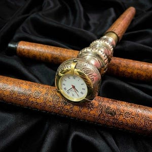 May include: A decorative walking cane with a built-in watch. The cane features a brown wooden shaft with a detailed pattern and a silver and gold-toned metal handle. The watch has a white face with Roman numerals.