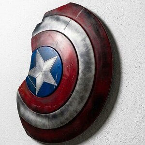 May include: A distressed Captain America shield, featuring a blue central disc with a white star, surrounded by concentric rings of red, silver, and dark red. The shield has a battle-worn appearance, with visible damage.