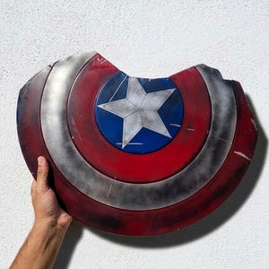 May include: A distressed Captain America shield, featuring a red, white, and blue color scheme. The shield has a central blue circle with a white star, surrounded by red and silver concentric rings. The shield has a damaged appearance.