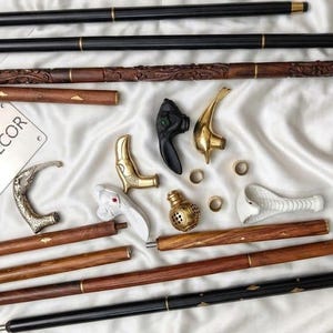 May include: A collection of walking stick components including long black and brown wooden shafts, various ornate metal and white handles, small brass rings, and a rectangular metal plate with the text DRAGON FIRE DECOR engraved on it.