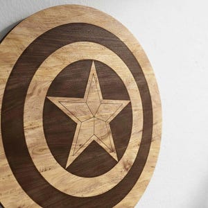 May include: A wooden Captain America shield with a star design. The shield is round with concentric circles in light and dark brown wood. A five-pointed star is in the center, also in light brown wood.