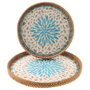May include: Two round decorative trays. Each tray features a mosaic design with a central blue floral pattern. The mosaic is set against a white background and framed by a woven, light brown border. The trays are stacked.