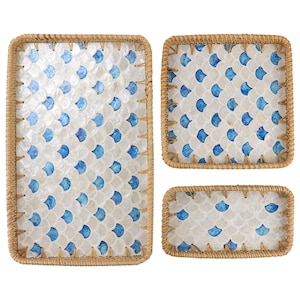 Può includere: Un set di tre vassoi decorativi con un motivo a conchiglie bianche e blu. I vassoi hanno una forma rettangolare con bordi marroni intrecciati. Il motivo a conchiglie è un disegno ripetuto di forme a conchiglia blu.