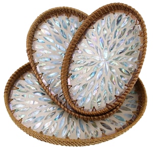 Op de afbeelding: Drie ovale decoratieve trays. Elke tray heeft een mozaïek van iriserende, bladvormige stukjes op een witte achtergrond. De randen zijn omlijst met geweven, lichtbruin rotan.