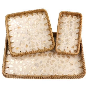 Pode incluir: Um conjunto de três bandejas de vime tecido. As bandejas têm formato quadrado, retangular e oblongo. O interior de cada bandeja apresenta uma superfície creme com um padrão floral feito de peças de concha iridescentes.
