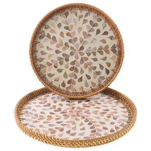 May include: Two round decorative trays. The trays have a woven, light brown border. The interior of the trays feature a pattern of small, light brown and beige shell-like shapes arranged in a floral design. The trays are stacked on top of each other.