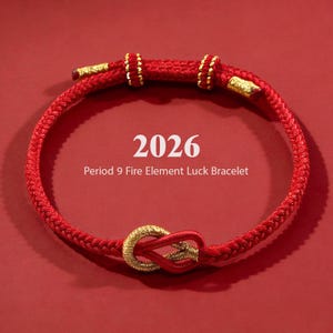 May include: A red braided bracelet with gold accents and a knot design. The bracelet features the text "2026 Period 9 Fire Element Luck Bracelet" in white. The bracelet is displayed on a red background.