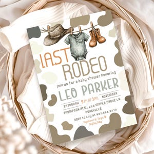 May include: A baby shower invitation with a western theme. The invitation features the text "LAST RODEO" in orange and brown, with illustrations of a cowboy hat, baby boots, and a onesie. The invitation is in a basket with baby clothes.