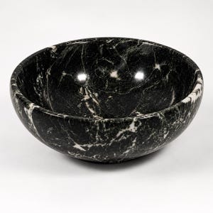 May include: A round bowl crafted from polished black marble, featuring prominent white veining throughout the surface. The bowl has a smooth, curved interior and a deep basin, showcasing the natural stone pattern with a glossy finish.