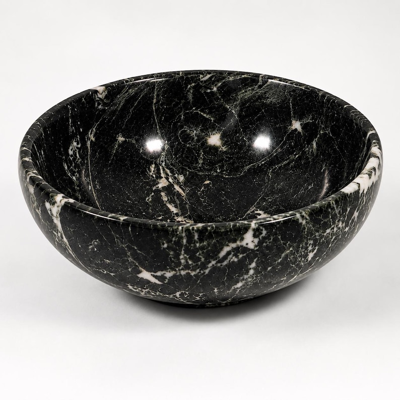May include: A round bowl crafted from polished black marble, featuring prominent white veining throughout the surface. The bowl has a smooth, curved interior and a deep basin, showcasing the natural stone pattern with a glossy finish.
