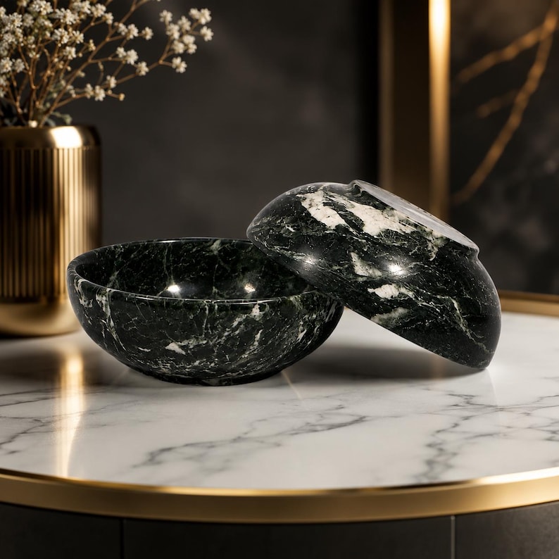 May include: Two round bowls crafted from dark green marble with prominent white veining. One bowl sits upright while the second bowl is tilted and resting against the first, showcasing the polished stone texture and natural marbled patterns.