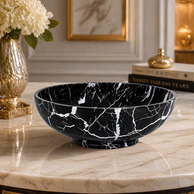 May include: A round, deep bowl featuring a black surface with prominent white veining throughout. The bowl has a smooth, polished finish and sits on a circular pedestal base, showcasing a high-contrast marble-like pattern across its exterior.