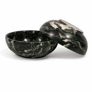 May include: Two dark green marble bowls with white veining. One bowl is positioned upright, while the second bowl is tilted and resting against the rim of the first. Both bowls feature a smooth, polished finish and a rounded, circular shape.