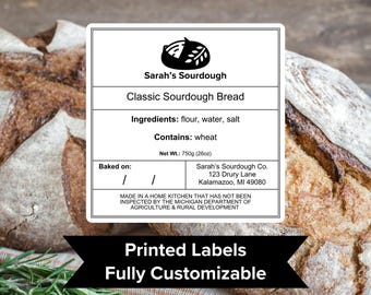 May include: A loaf of classic sourdough bread with a label that reads "Sarah's Sourdough." The label lists ingredients, net weight (26oz), and business information. The bottom of the label says "Printed Labels Fully Customizable."
