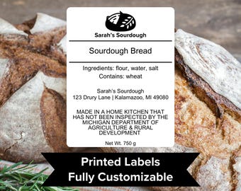 May include: A white label with black text for sourdough bread. The label includes the name "Sarah's Sourdough", the ingredients, and the statement "Made in a home kitchen that has not been inspected by the Michigan Department of Agriculture & Rural Development". The label also includes the net weight of 750 grams. The label is placed on top of a loaf of sourdough bread.