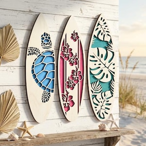 May include: Three wooden surfboards with decorative cutouts. One features a blue turtle design, another has pink hibiscus flowers, and the third showcases green tropical leaves. The surfboards are displayed on a wooden shelf with beach-themed decor.