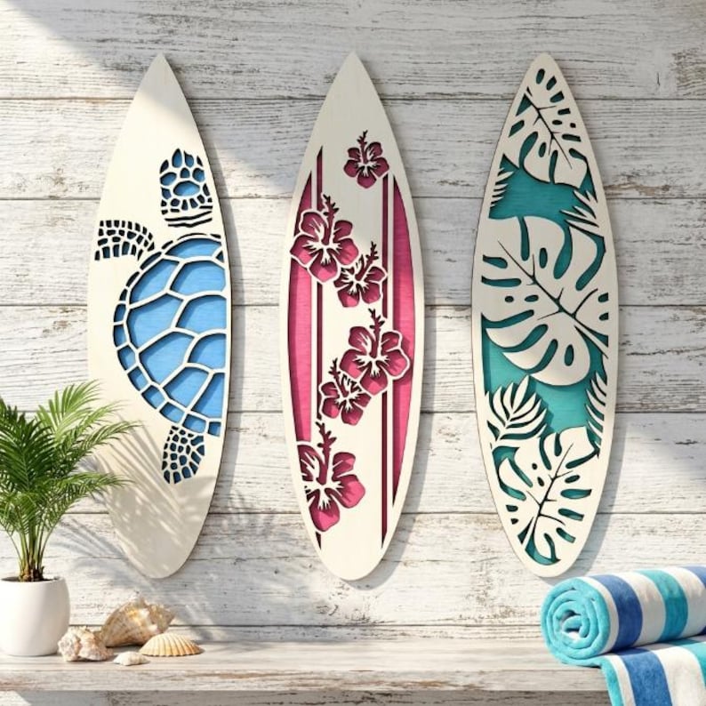 May include: Three decorative wooden surfboards with cut-out designs. One features a blue sea turtle, another has pink hibiscus flowers, and the third showcases tropical leaves. The surfboards are mounted on a white wooden wall, evoking a beach theme.