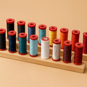May include: A collection of colorful thread spools with red tops, arranged on a wooden display. The spools are in various colors, including black, navy, teal, light blue, yellow, orange, and red. A needle is inserted in one of the white spools.