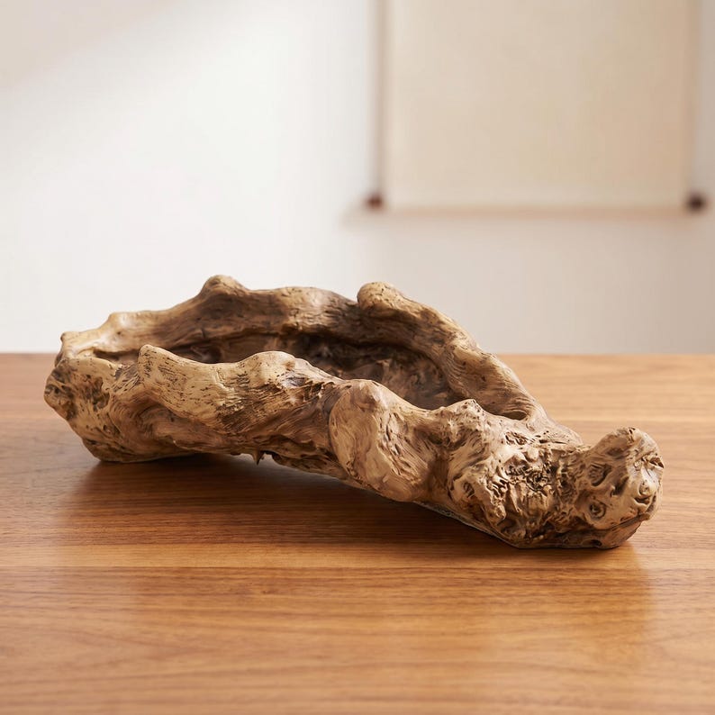 Puede incluir: Un cuenco decorativo de madera oblongo con un aspecto natural y envejecido. El cuenco es de color marr&oacute;n claro con acentos marrones m&aacute;s oscuros y tiene una superficie rugosa y texturizada. El cuenco est&aacute; colocado sobre una mesa de madera.