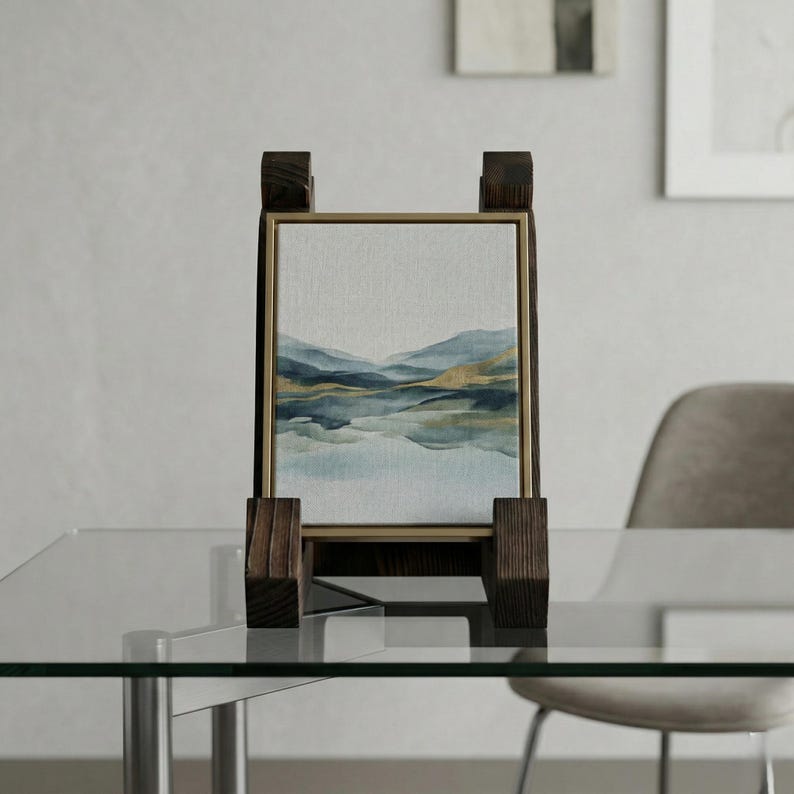 Puede incluir: Una pintura de paisaje enmarcada con un borde dorado, exhibida en un caballete de madera. La obra de arte representa una serena escena lacustre con tonos azules y dorados. El caballete es de madera oscura y tiene un dise&ntilde;o simple y moderno.