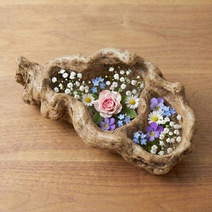 Puede incluir: Un cuenco decorativo de madera r&uacute;stica lleno de una variedad de flores coloridas. El arreglo incluye una rosa rosa, margaritas blancas, nomeolvides azules y pensamientos morados. El cuenco est&aacute; sobre una superficie de madera.