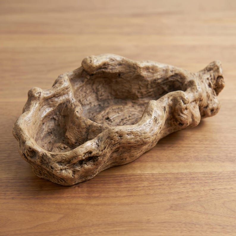 Puede incluir: Un cuenco decorativo con aspecto de madera flotante. El cuenco marr&oacute;n claro tiene una forma irregular y una superficie texturizada. Presenta una depresi&oacute;n central.