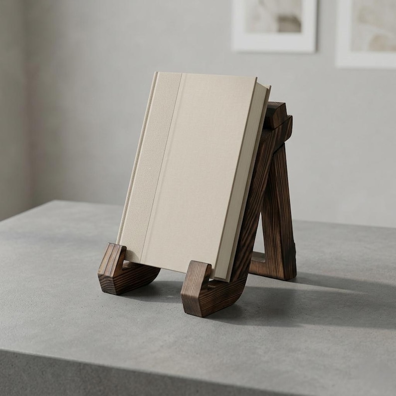 Puede incluir: Un atril de madera marr&oacute;n oscuro sostiene un libro beige. El atril est&aacute; inclinado, con una base curva y soportes. El libro est&aacute; en posici&oacute;n vertical, con una cubierta texturizada. El atril est&aacute; sobre una superficie gris.