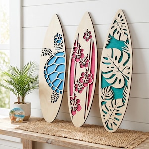 May include: Three wooden surfboards with laser-cut designs. One features a turtle, another hibiscus flowers, and the third tropical leaves. Each board has a light wood finish with colorful accents of blue, pink, and teal.