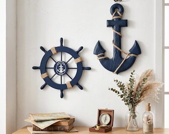 May include: Nautical-themed wall decor featuring a navy blue ship's wheel and anchor. The ship's wheel has a rope accent and an anchor emblem in the center. The anchor is also navy blue with rope detailing. The items are mounted on a white wall.
