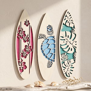 May include: Three wooden surfboards with decorative cutouts. One features pink hibiscus flowers, another a blue sea turtle, and the third has green and white tropical leaves. The surfboards are displayed against a neutral background.