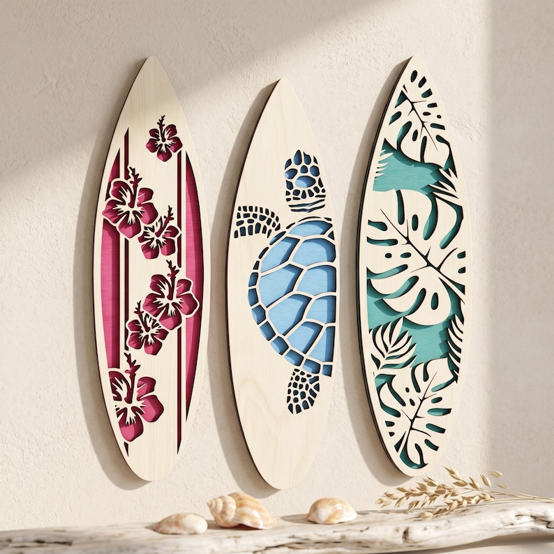 May include: Three wooden surfboards with decorative cutouts. One features pink hibiscus flowers, another a blue sea turtle, and the third has green and white tropical leaves. The surfboards are displayed against a neutral background.