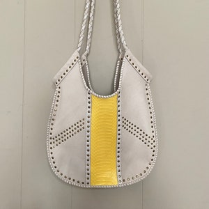 Peut inclure: Un sac cabas en cuir blanc avec un panneau en peau de serpent jaune et des bretelles tressées blanches. Le sac a un design unique avec un bord festonné et des rangées de clous argentés.