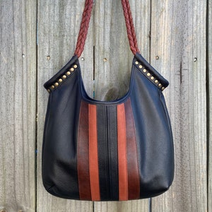 May include: A black leather tote bag with brown and orange stripes and gold studs. The bag has braided leather straps.