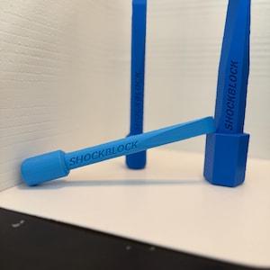 Könnte beinhalten: Drei leuchtend blaue Kunststoffwerkzeuge mit keilförmiger Spitze und texturierter Basis. Jedes Werkzeug trägt den Schriftzug SHOCKBLOCK in geprägten Großbuchstaben an der Seite. Die Objekte sind in einer Gruppe angeordnet, wobei eines waagerecht liegt.