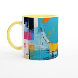Puede incluir: Una taza de café de cerámica con asa e interior amarillos. El exterior presenta un diseño abstracto con formas azules, naranjas, rosas y negras. La taza es blanca con un acabado brillante.
