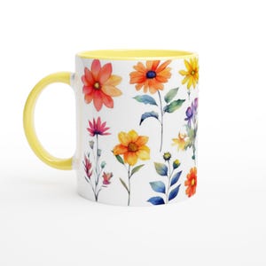 Puede incluir: Taza de cerámica blanca con asa e interior amarillos, decorada con flores de acuarela en tonos naranja, amarillo, rosa y morado. Las flores están sobre un fondo blanco.